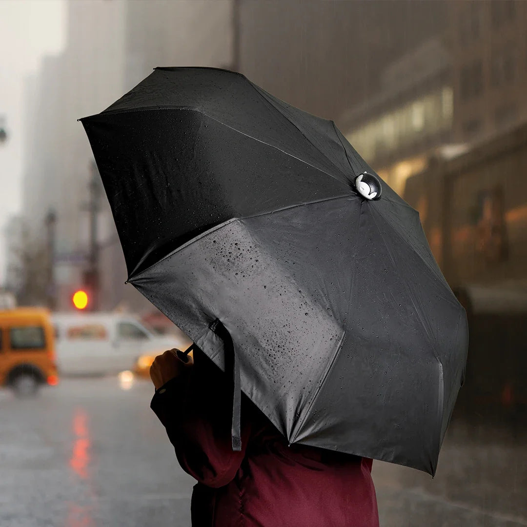 A person with a Spookula umbrella on a rainy city street, blurred buildings and cars in the backdrop.